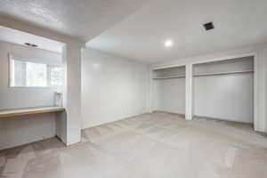 Unfurnished bedroom featuring light colored carpet, built in desk, a textured ceiling, and multiple closets