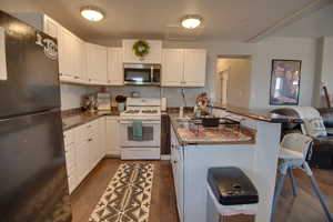 Kitchen featuring black fridge, gas range gas stove, dark wood-type flooring, sink, and white cabinetry