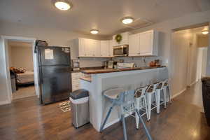 Kitchen with a breakfast bar, black refrigerator, white cabinets, and dark hardwood / wood-style floors