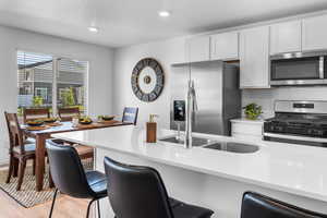 Kitchen featuring a kitchen breakfast bar, light wood-type flooring, stainless steel appliances, sink, and white cabinets