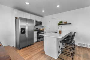 Kitchen with sink, kitchen peninsula, a breakfast bar area, white cabinets, and appliances with stainless steel finishes