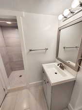 Bathroom featuring tiled shower, vanity, and tile patterned flooring