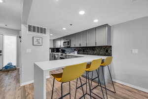 Kitchen with kitchen peninsula, appliances with stainless steel finishes, light hardwood / wood-style floors, and gray cabinetry