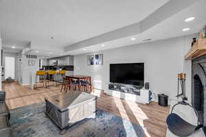 Living room with bar area, a fireplace, and light wood-type flooring