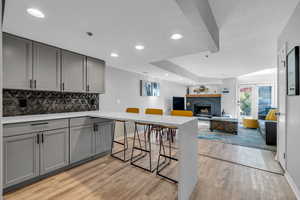 Kitchen with gray cabinetry, tasteful backsplash, a fireplace, and light hardwood / wood-style flooring