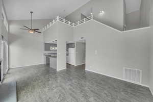 Unfurnished living room featuring dark hardwood / wood-style floors, high vaulted ceiling, and ceiling fan