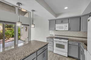 Kitchen with dark stone countertops, pendant lighting, white appliances, light hardwood / wood-style floors, and gray cabinets