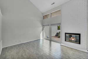 Unfurnished living room featuring hardwood / wood-style floors, a fireplace, and high vaulted ceiling