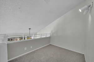 Spare room featuring carpet floors, a textured ceiling, and vaulted ceiling