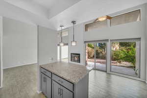 Kitchen with hanging light fixtures, gray cabinets, light wood-type flooring, a fireplace, and light stone counters