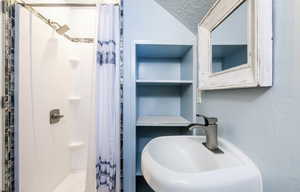 Full bathroom featuring curtained shower, vaulted ceiling, a textured ceiling, and a sink
