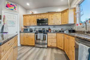 Kitchen with sink, stainless steel appliances, dark stone counters, and light hardwood / wood-style flooring