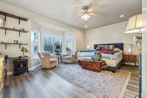 Main Level Primary Bedroom featuring hardwood / wood-style floors, a wood stove, and ceiling fan