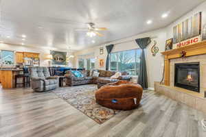 Living room with ceiling fan with notable chandelier, light hardwood / wood-style floors, a textured ceiling, and a tile fireplace