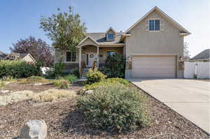 View of front of house with stucco siding, stone siding, fence, concrete driveway, and a garage