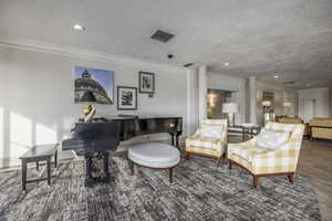 Sitting room with a textured ceiling, dark hardwood / wood-style floors, decorative columns, and crown molding