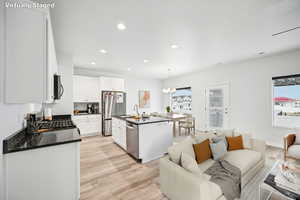 Kitchen featuring appliances with stainless steel finishes, decorative light fixtures, white cabinets, a kitchen island with sink, and plenty of natural light