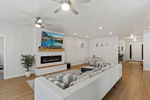 Living room with a fireplace, light hardwood / wood-style floors, and ceiling fan