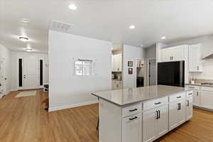 Kitchen featuring black fridge, light hardwood / wood-style flooring, white cabinets, a kitchen island, and stainless steel gas stovetop