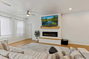 Living room featuring ceiling fan, a fireplace, and light hardwood / wood-style floors