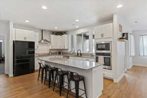 Kitchen featuring sink, wall chimney exhaust hood, stainless steel appliances, a kitchen breakfast bar, and a kitchen island