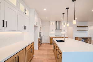 Kitchen with a sink, oven, backsplash, wall chimney range hood, and light wood-style floors
