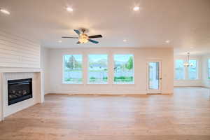 Unfurnished living room featuring a wealth of natural light, a tiled fireplace, baseboards, and ceiling fan with notable chandelier