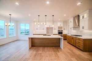 Kitchen featuring recessed lighting, stainless steel oven, a sink, wall chimney range hood, and tasteful backsplash