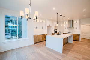 Kitchen with oven, wall chimney range hood, cooktop, and light wood-style floors