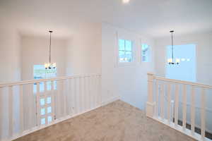 Hallway featuring a chandelier, an upstairs landing, and carpet floors