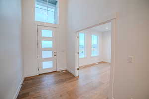 Foyer entrance with light wood-type flooring, baseboards, and a towering ceiling