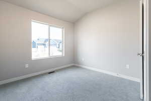 Carpeted spare room featuring lofted ceiling