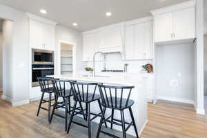 Kitchen featuring white cabinetry, light hardwood / wood-style flooring, a center island with sink, black microwave, and wall oven