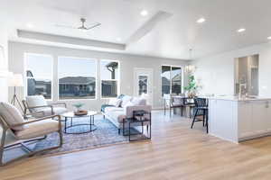 Living room featuring ceiling fan with notable chandelier, sink, a tray ceiling, and light hardwood / wood-style floors