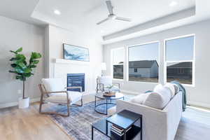 Living room with a raised ceiling, ceiling fan, and light wood-type flooring