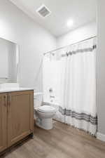 Full bathroom with vanity, hardwood / wood-style floors, shower / bath combination with curtain, and toilet