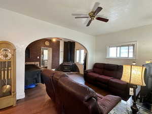 Living room featuring a textured ceiling, dark hardwood / wood-style flooring, a wood stove, and ceiling fan