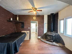 Bedroom featuring brick wall, a textured ceiling, ceiling fan, hardwood / wood-style floors, and a wood stove