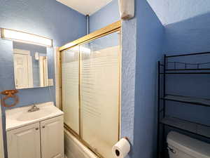 Full bathroom with a textured ceiling, vanity, toilet, and bath / shower combo with glass door