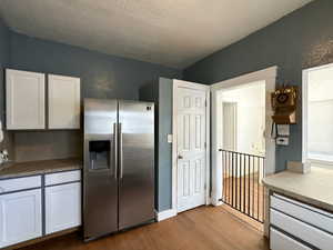 Kitchen featuring stainless steel fridge with ice dispenser, a textured ceiling, white cabinetry, and hardwood / wood-style floors