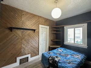 Bedroom featuring a textured ceiling, hardwood / wood-style flooring, and wooden walls