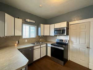 Kitchen with sink, dark hardwood / wood-style floors, a textured ceiling, white cabinets, and appliances with stainless steel finishes