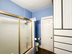 Bathroom featuring bath / shower combo with glass door, wood-type flooring, a textured ceiling, and toilet