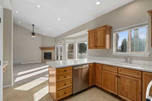 Kitchen featuring sink, stainless steel dishwasher, kitchen peninsula, lofted ceiling, and a fireplace