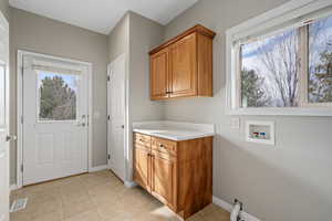 Clothes washing area featuring hookup for a washing machine, light tile patterned flooring, and cabinets