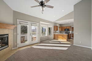 Unfurnished living room featuring a tile fireplace, light carpet, french doors, and high vaulted ceiling