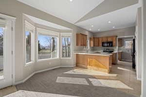 Kitchen featuring kitchen peninsula, a kitchen breakfast bar, stainless steel appliances, light tile patterned floors, and lofted ceiling