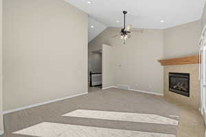 Unfurnished living room with a tile fireplace, light carpet, vaulted ceiling, and ceiling fan