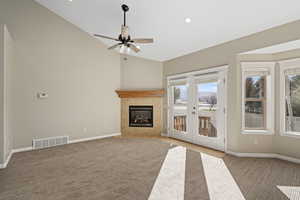 Unfurnished living room with a tiled fireplace, ceiling fan, french doors, and light colored carpet