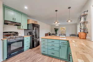 Kitchen featuring pendant lighting, black appliances, green cabinetry, light wood-type flooring, and butcher block countertops